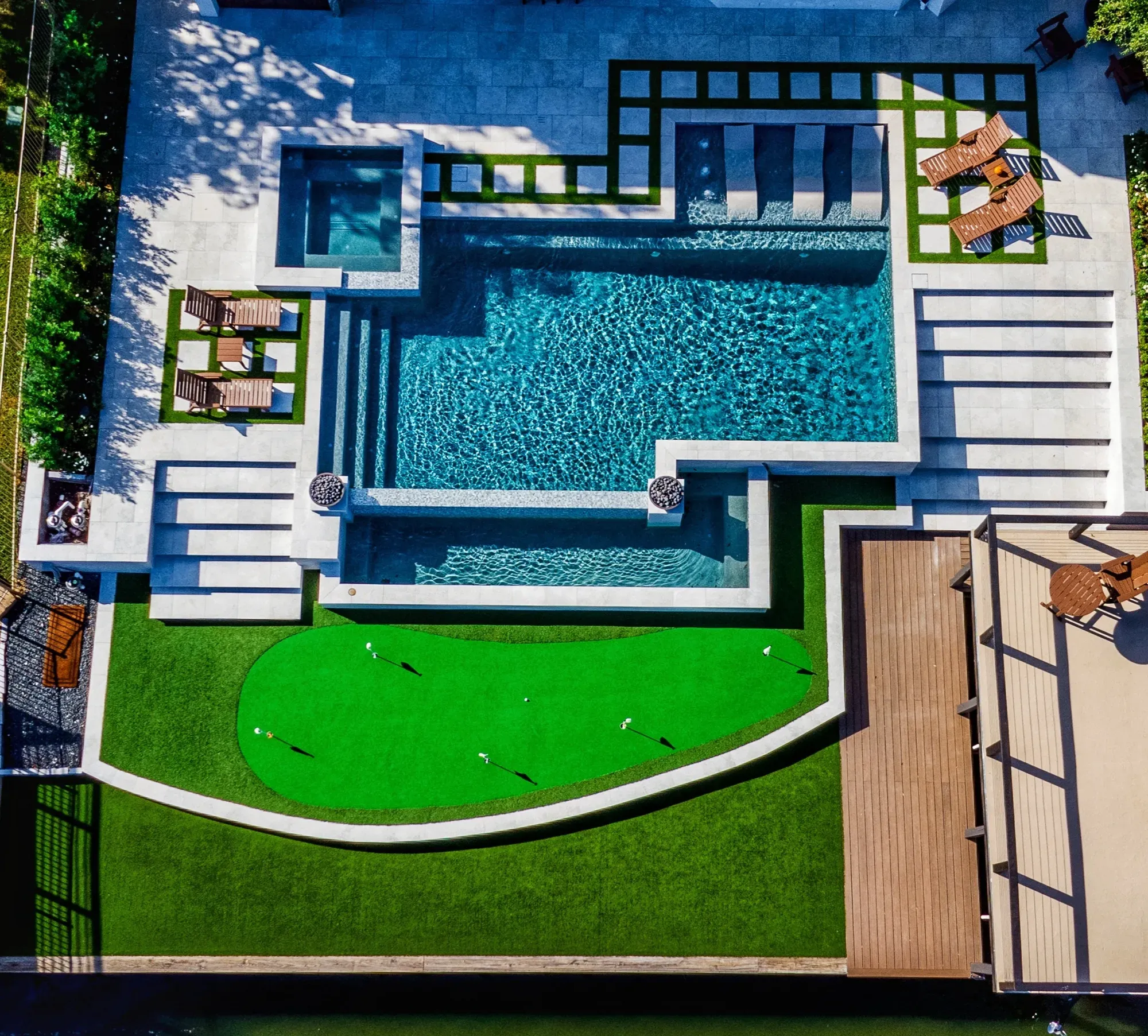 An overhead view of a three-level backyard with a pool, paver-and-turf terraces and a curved practice green