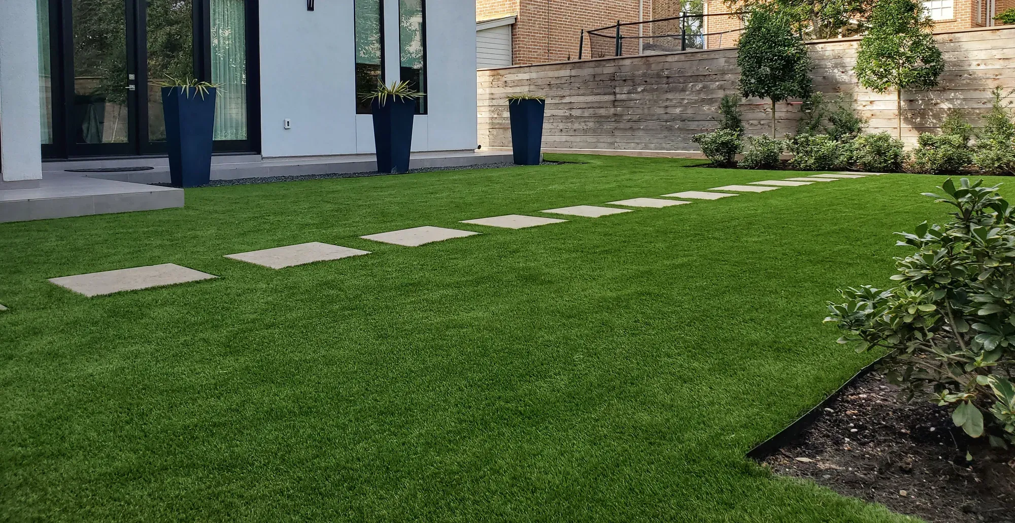 An artificial lawn with stone treads leading to a modern house and a stone boundary wall