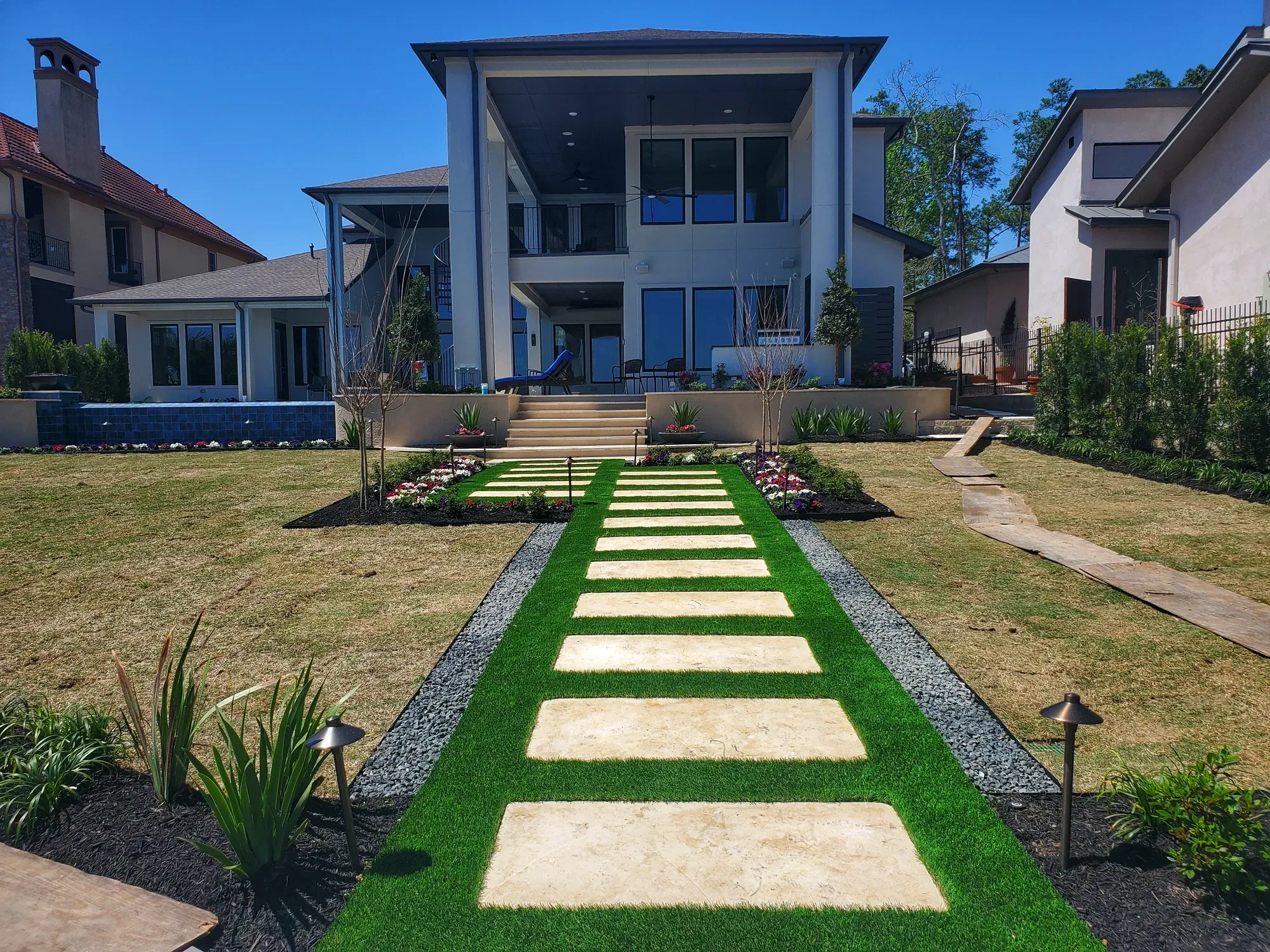 A path of large stone treads with artificial turf between them leading to the front door of a modern home