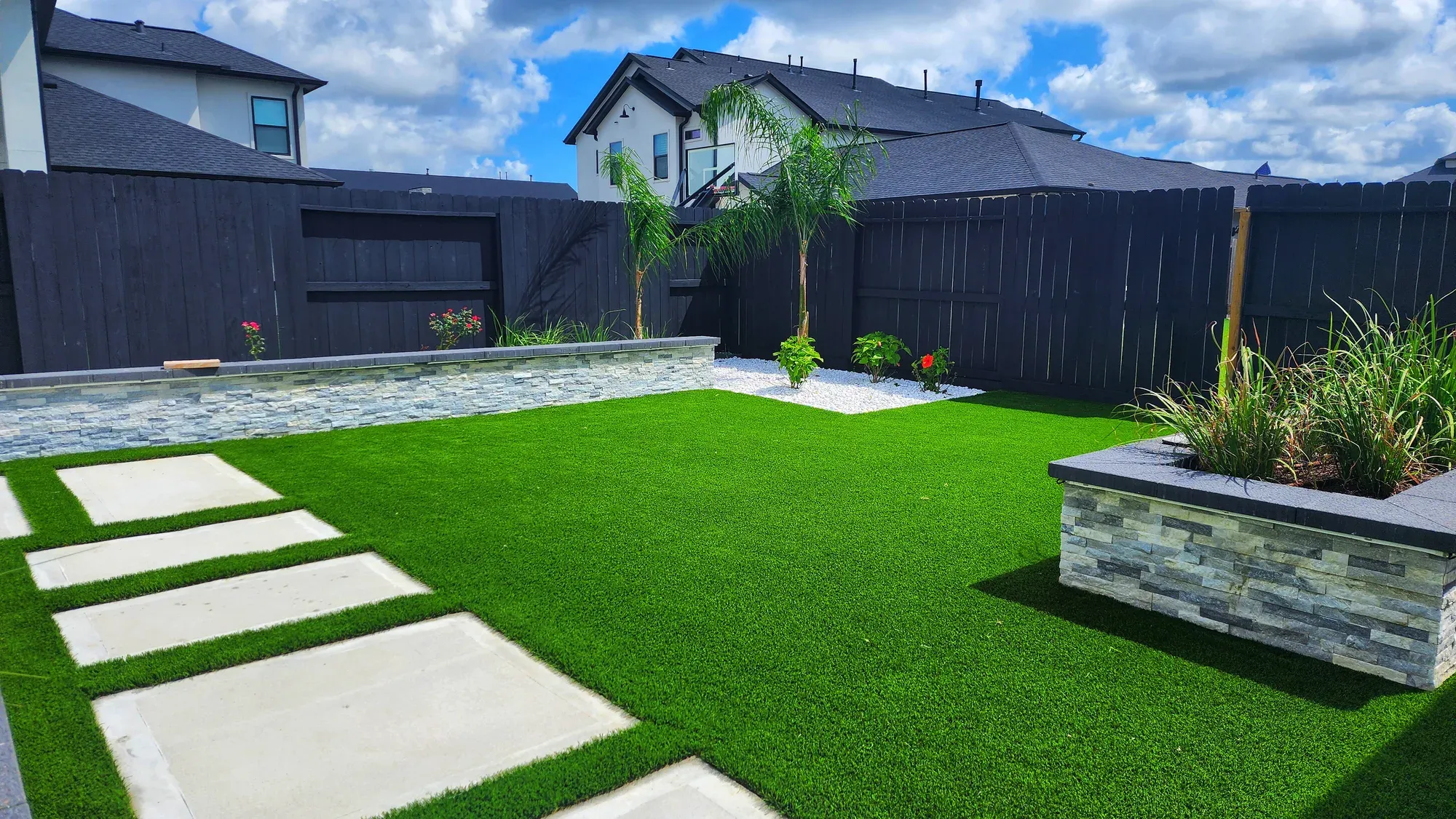 Stone treads set into an artificial lawn beside a dark fence and a modern house