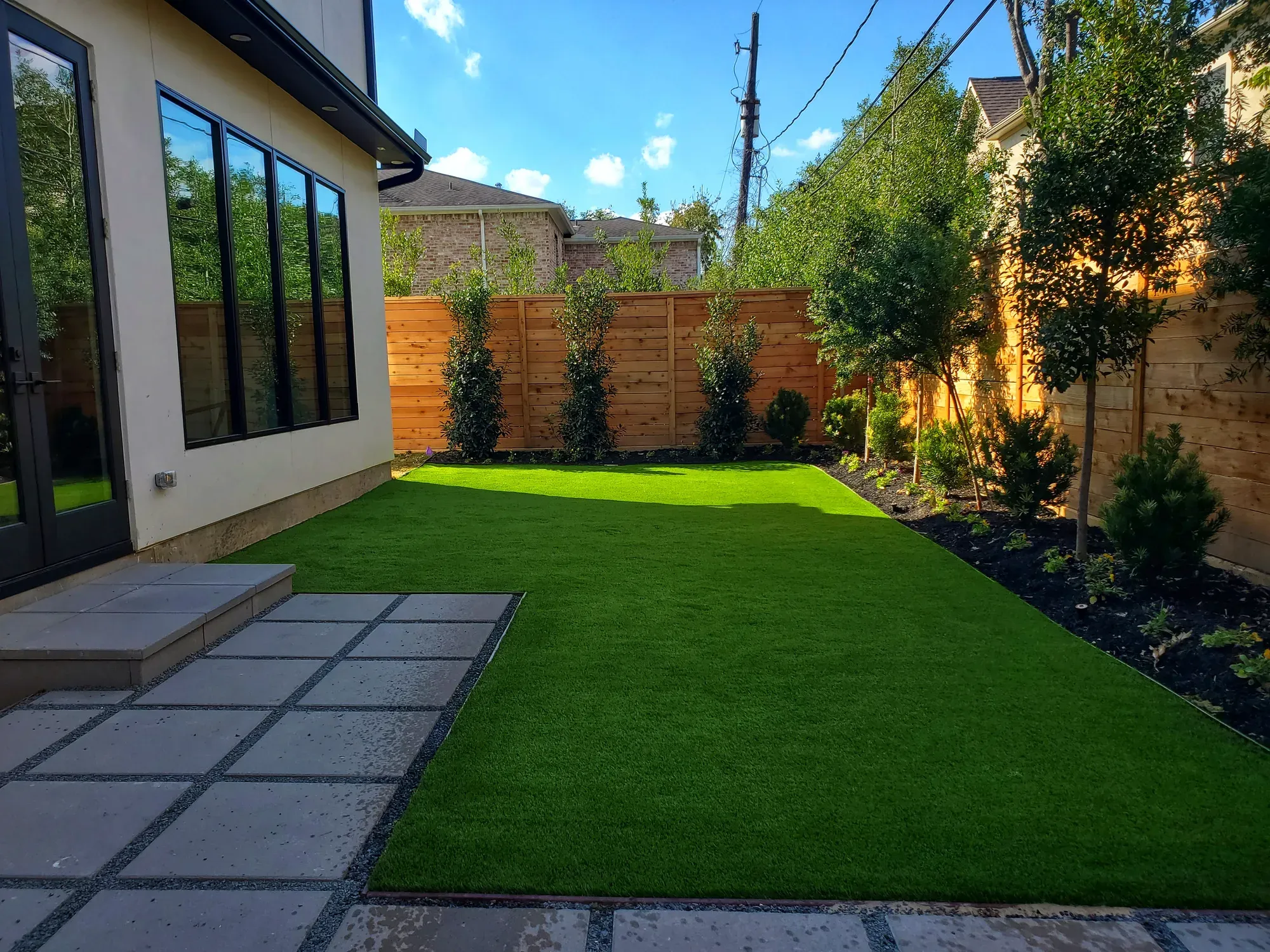 The same lawn in evening light, with dark planters and a timber screen
