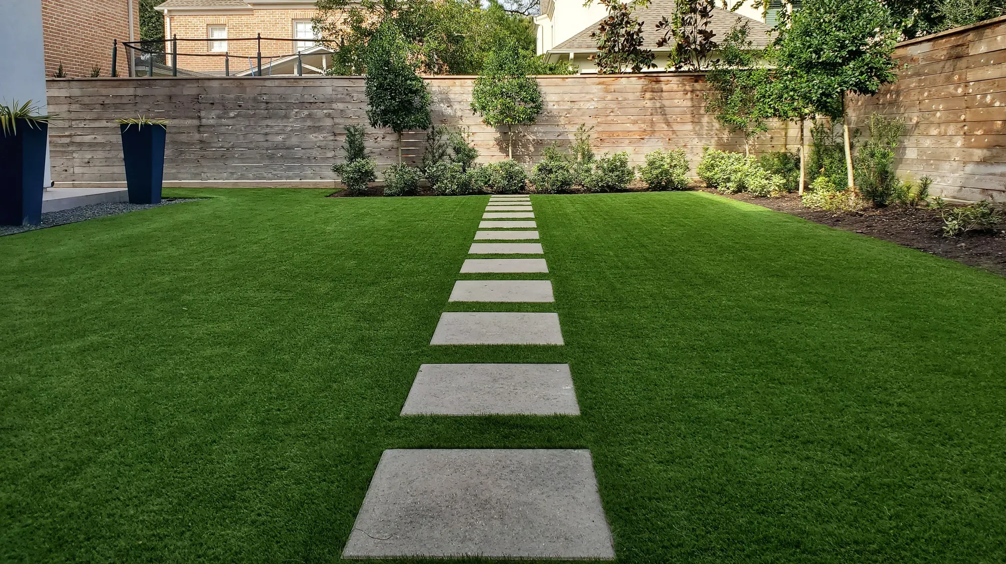 Stone treads set into an artificial lawn between clipped trees and a stone wall