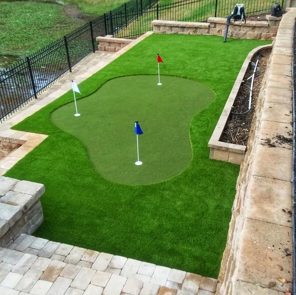 A three-hole practice green with red, white and blue flags, built into a walled raised terrace