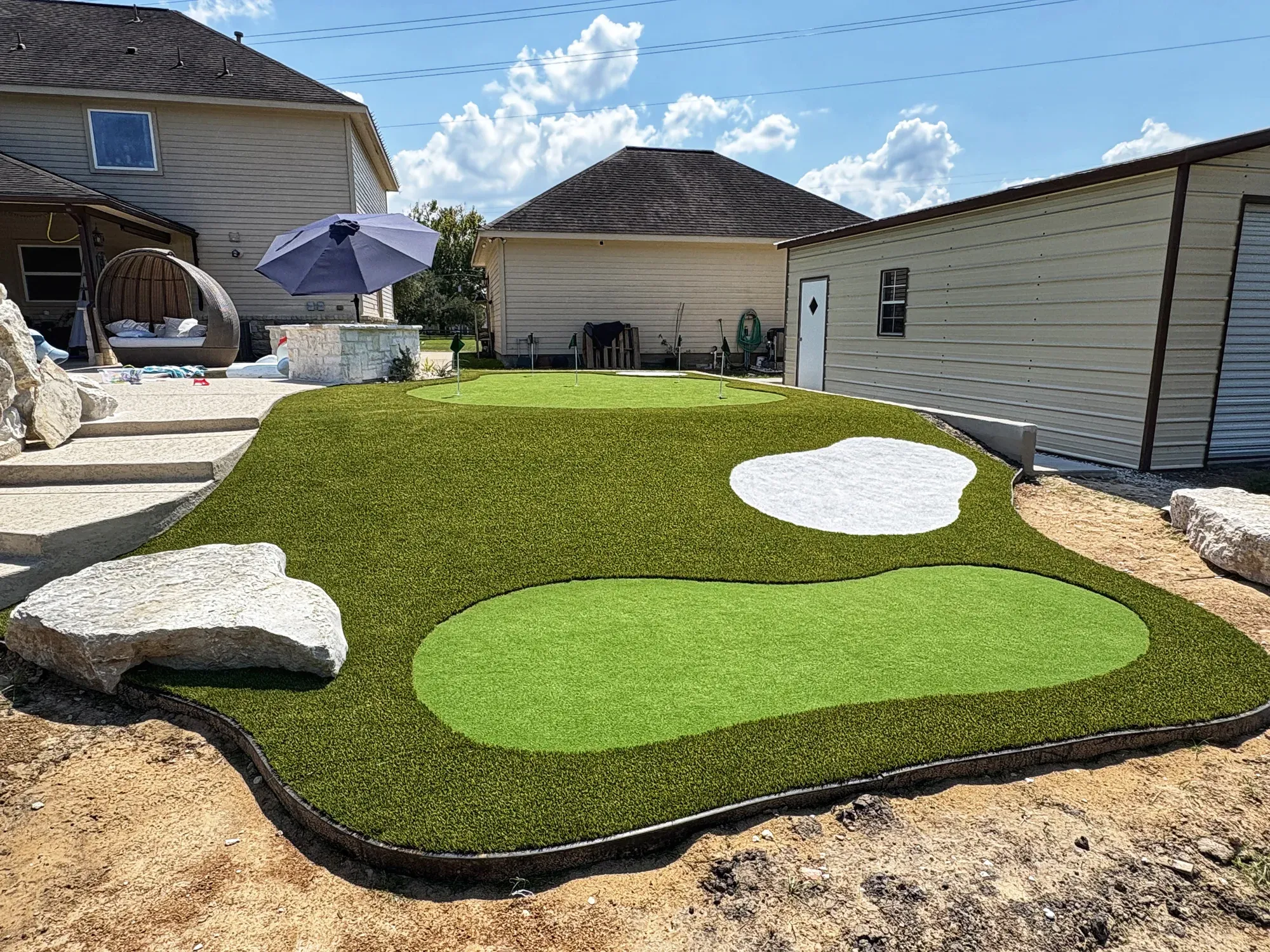 The practice green and its sand bunker from the drive, boulders along the edge