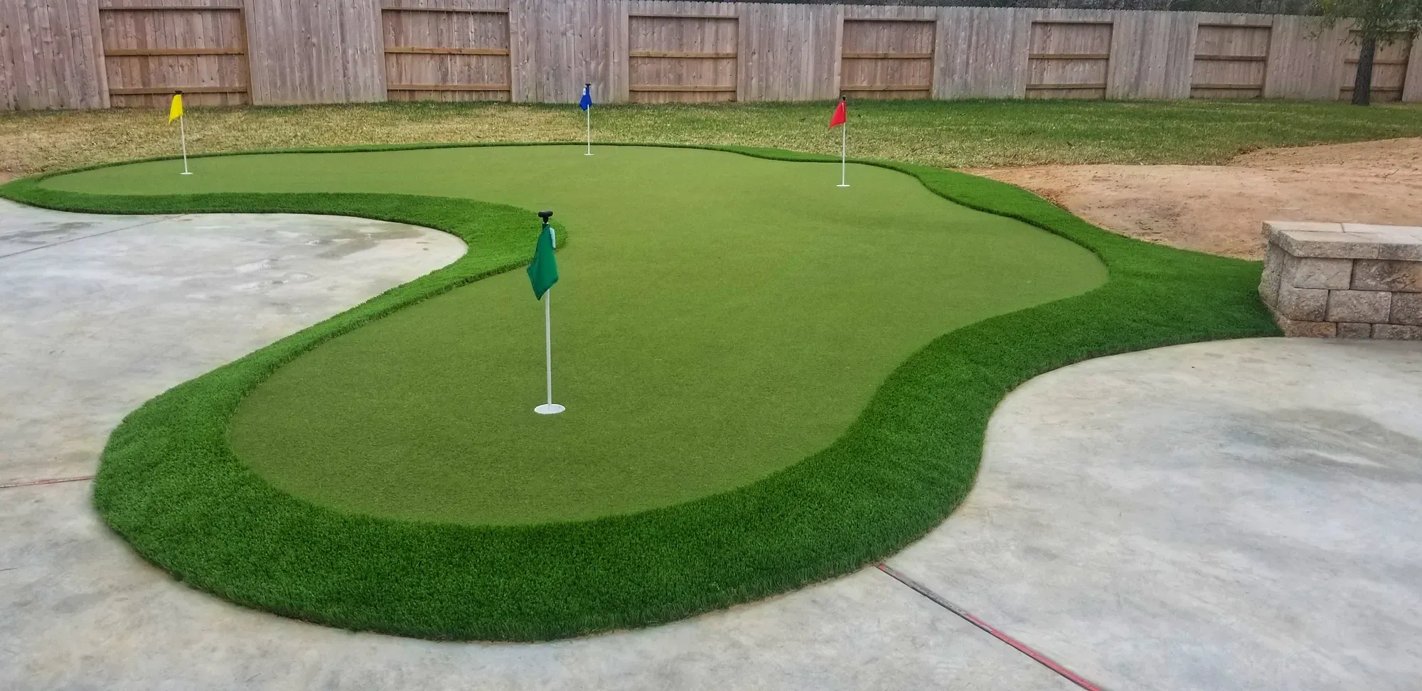 A curved practice green with a flag, set against a concrete patio