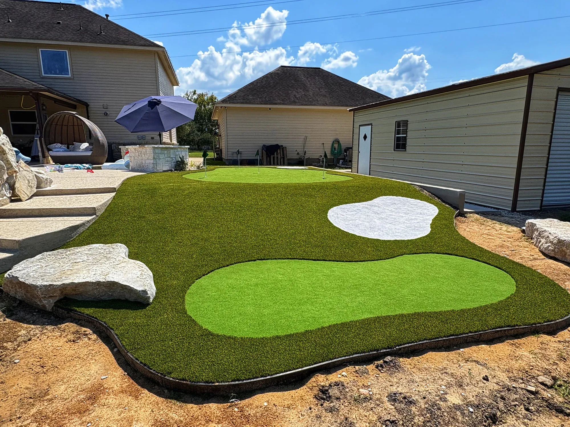 A shaped putting green with a white sand bunker, set into a boulder-edged bed