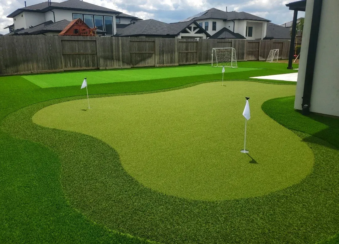 A free-form practice green with flags in a fenced back garden