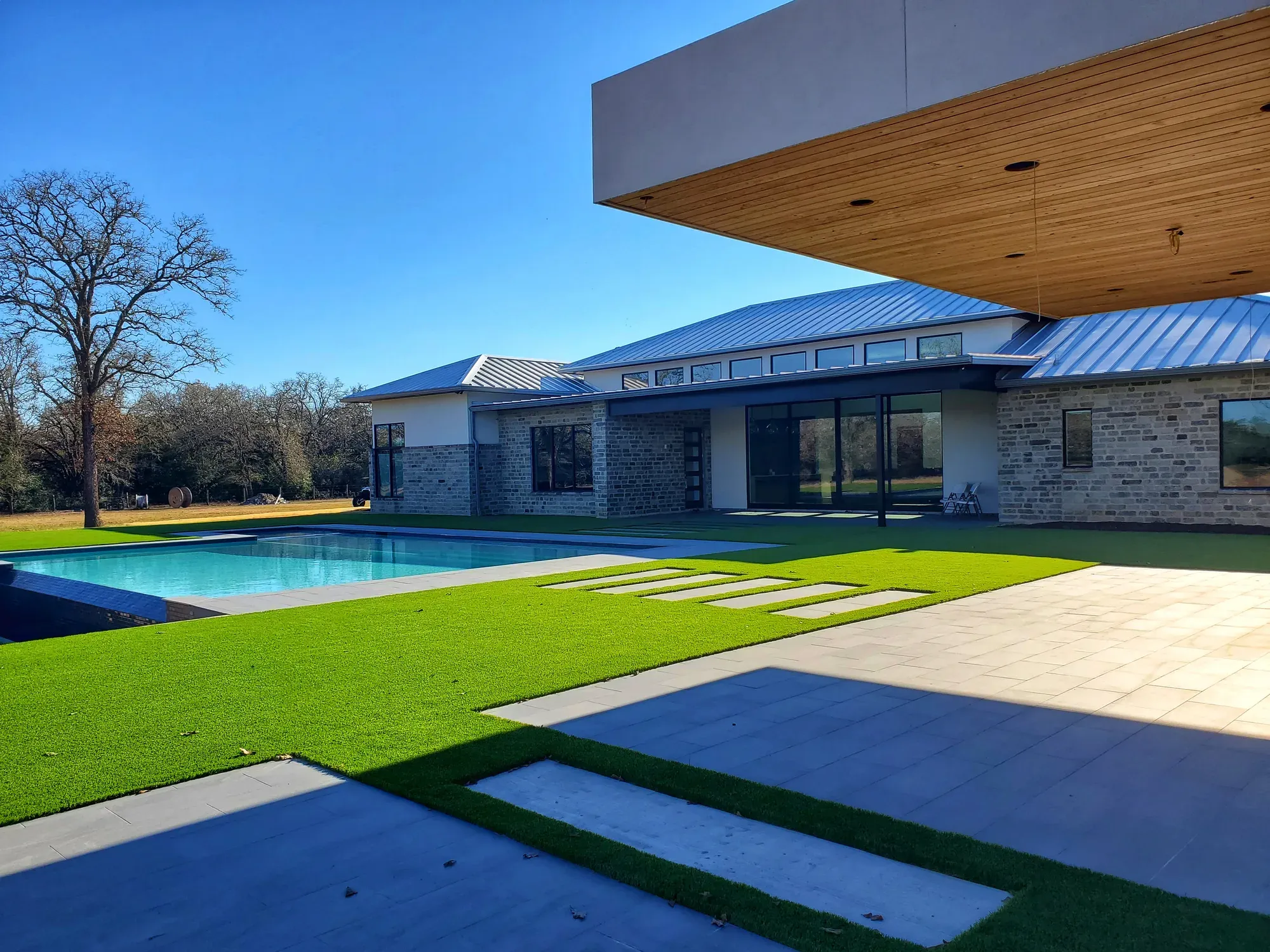 An artificial turf lawn with stone stepping stones running alongside a long modern pool