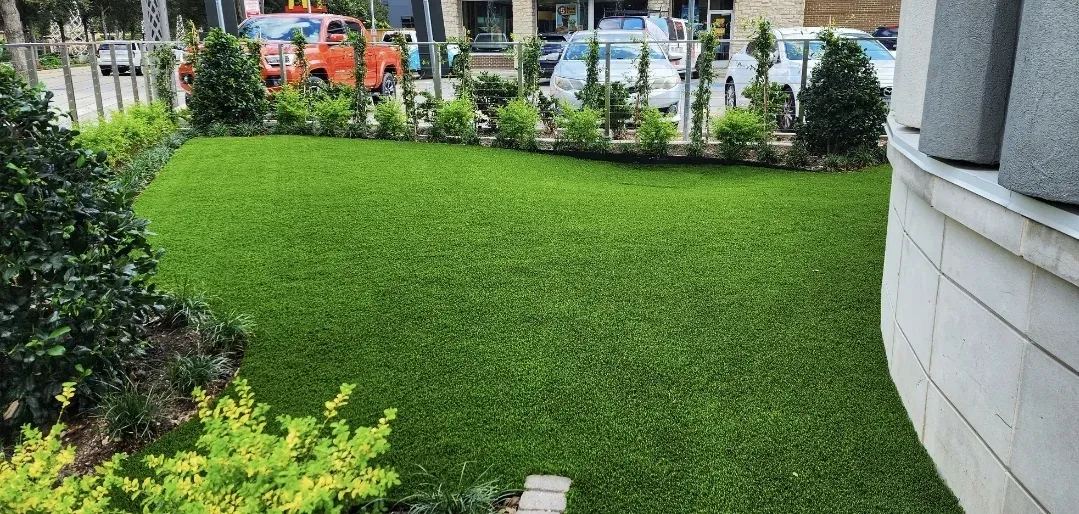 A strip of artificial turf lawn along a building frontage with parked cars behind