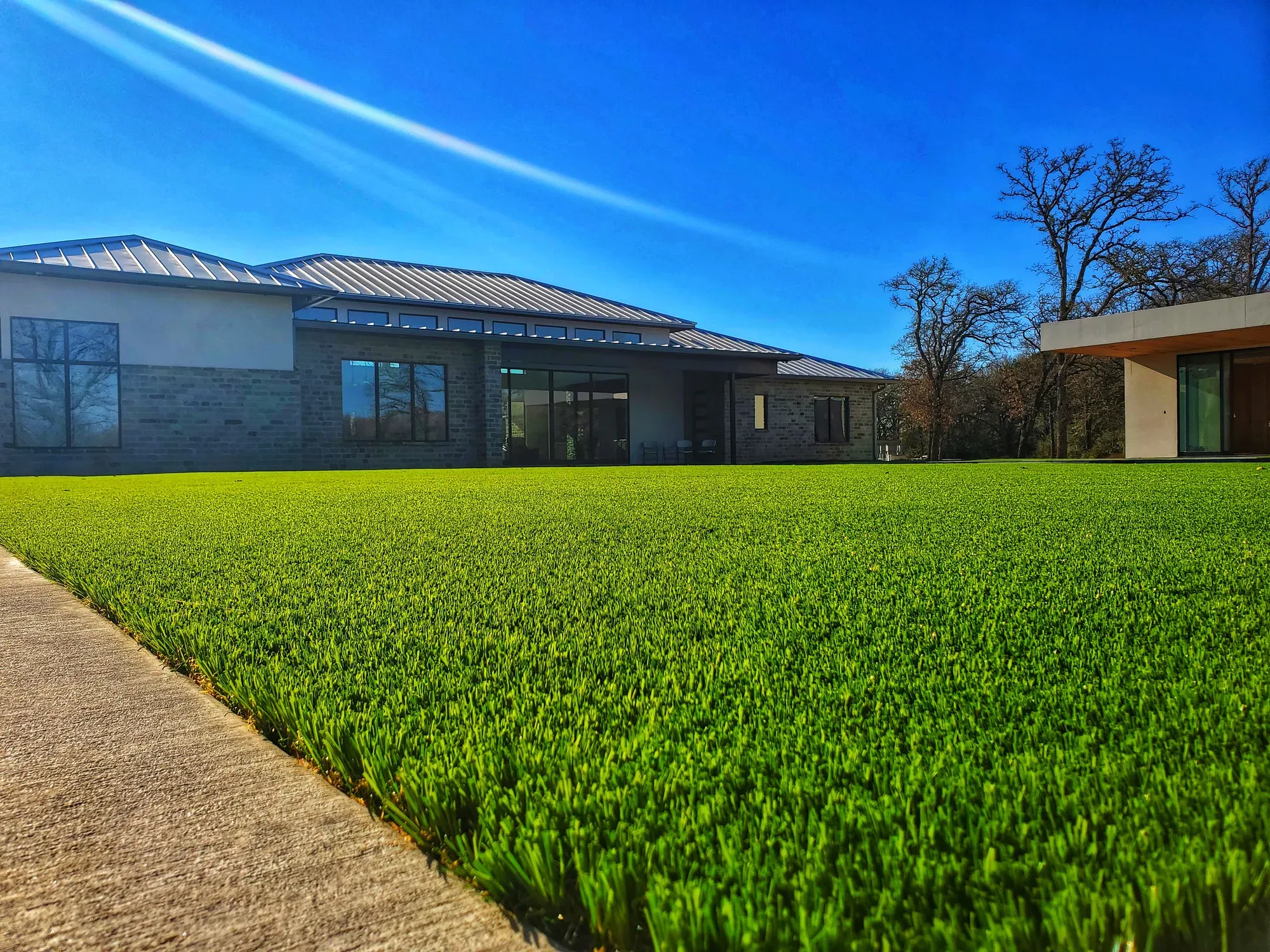Low view across a dense artificial turf lawn with the blades standing upright, house behind