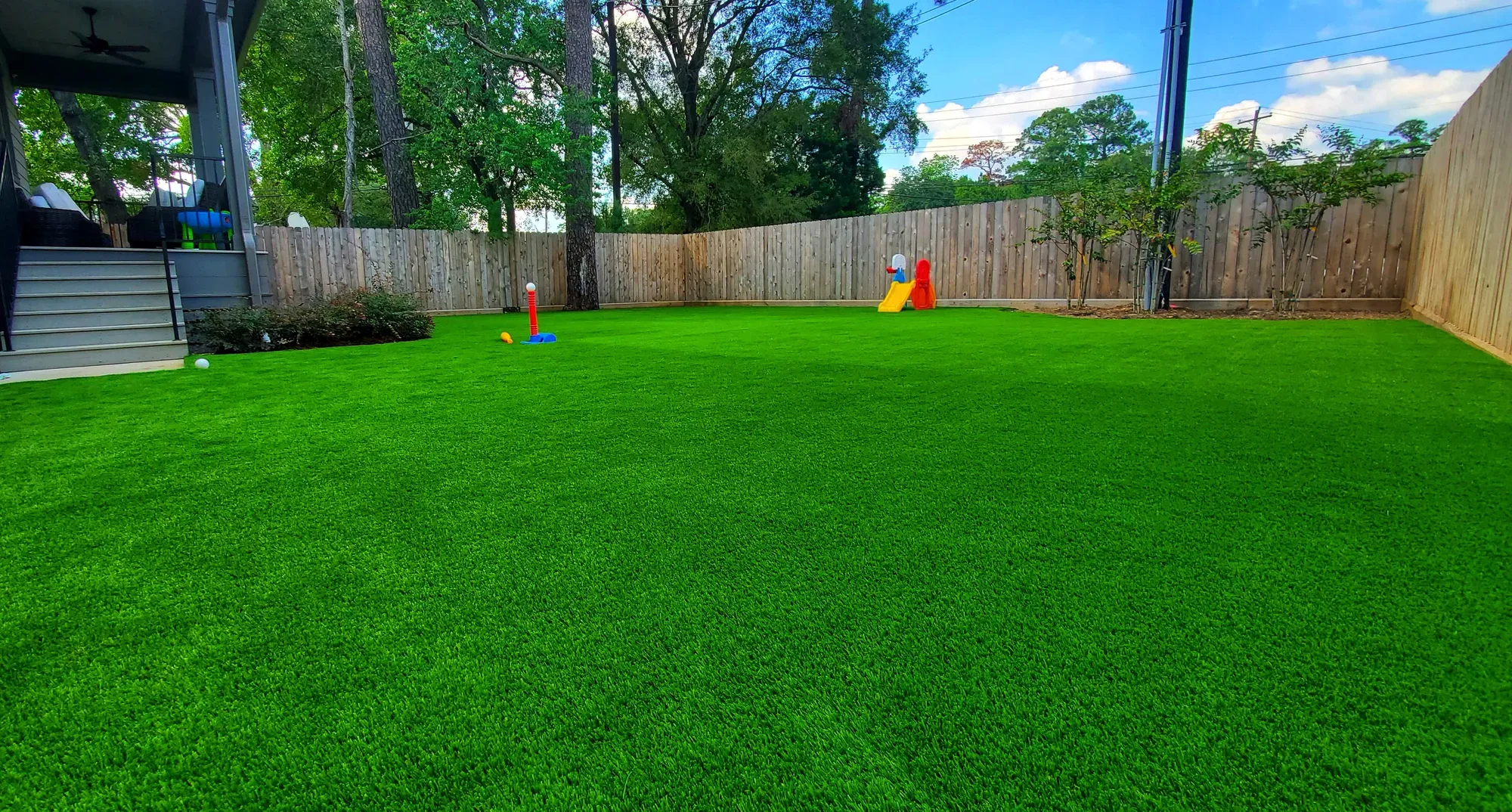 Backyard at dusk with a lit swimming pool and water feature wall, a fire pit lounge, a covered patio and a putting green on the lawn