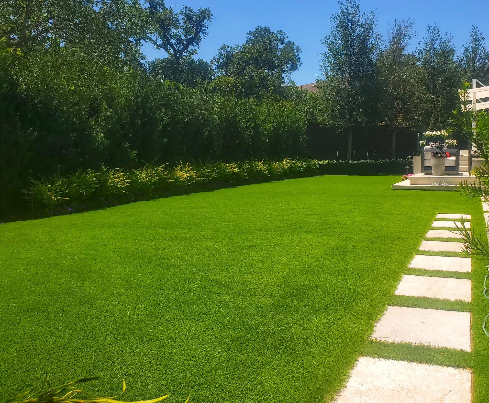 Level artificial turf lawn edged with stepping stones and a clipped hedge in a back yard