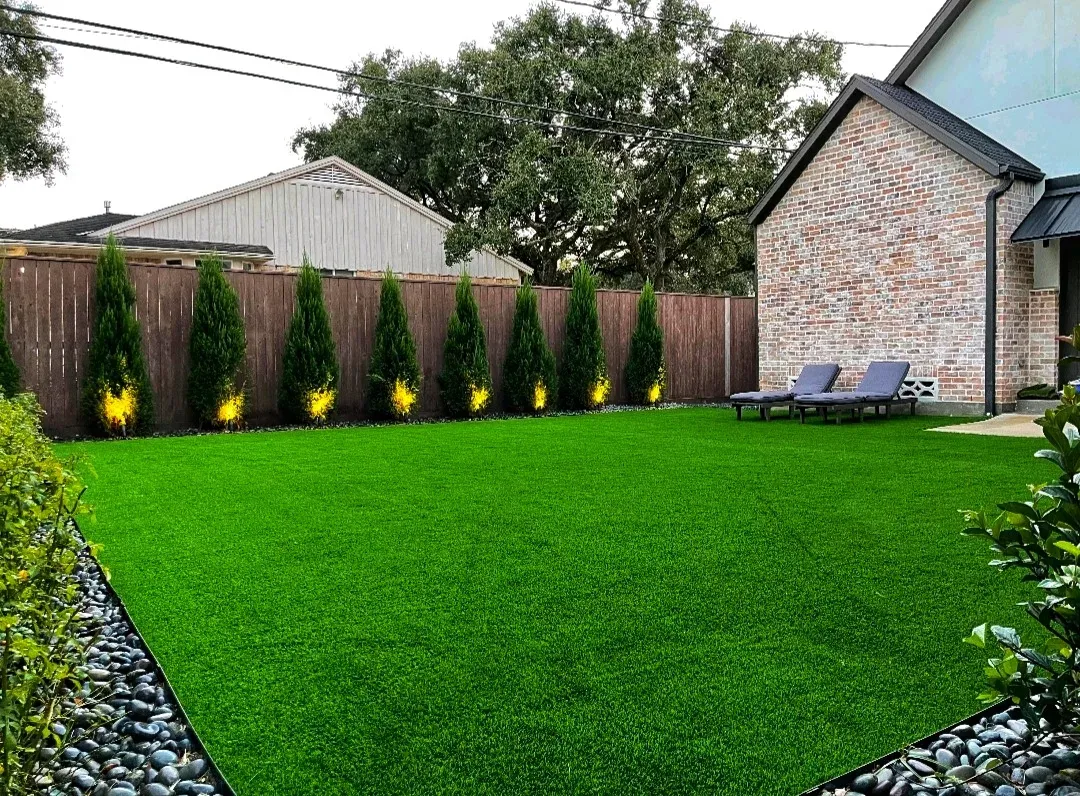 An artificial lawn edged with river rock and clipped shrubs against a brick wall
