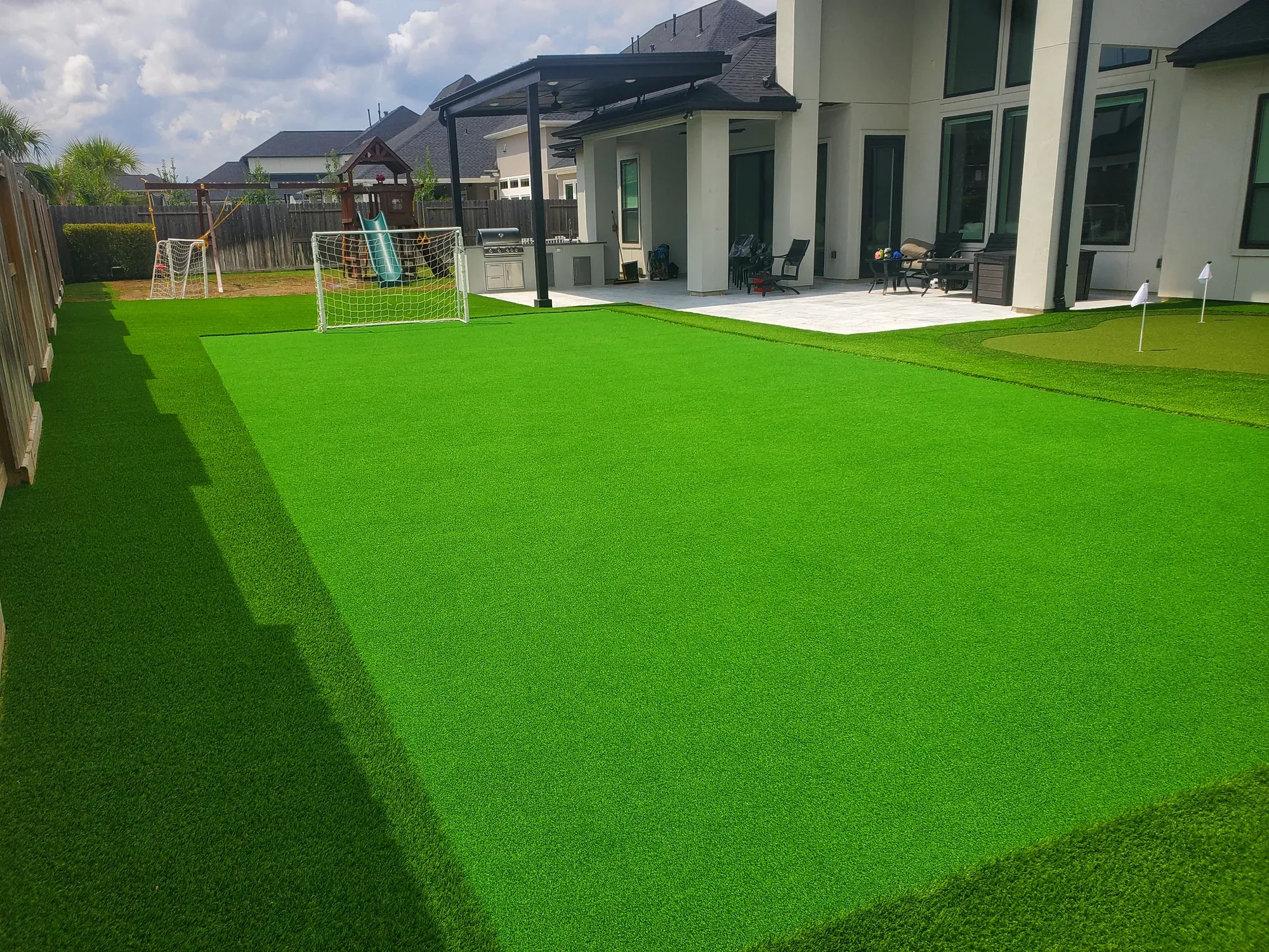 Large artificial turf back lawn with a soccer goal at one end and a putting green at the other, behind a two-storey house