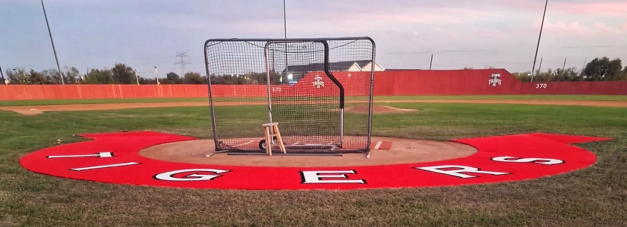 High school baseball field with the team name cut into artificial turf in a red ring around the pitching mound, outfield wall behind