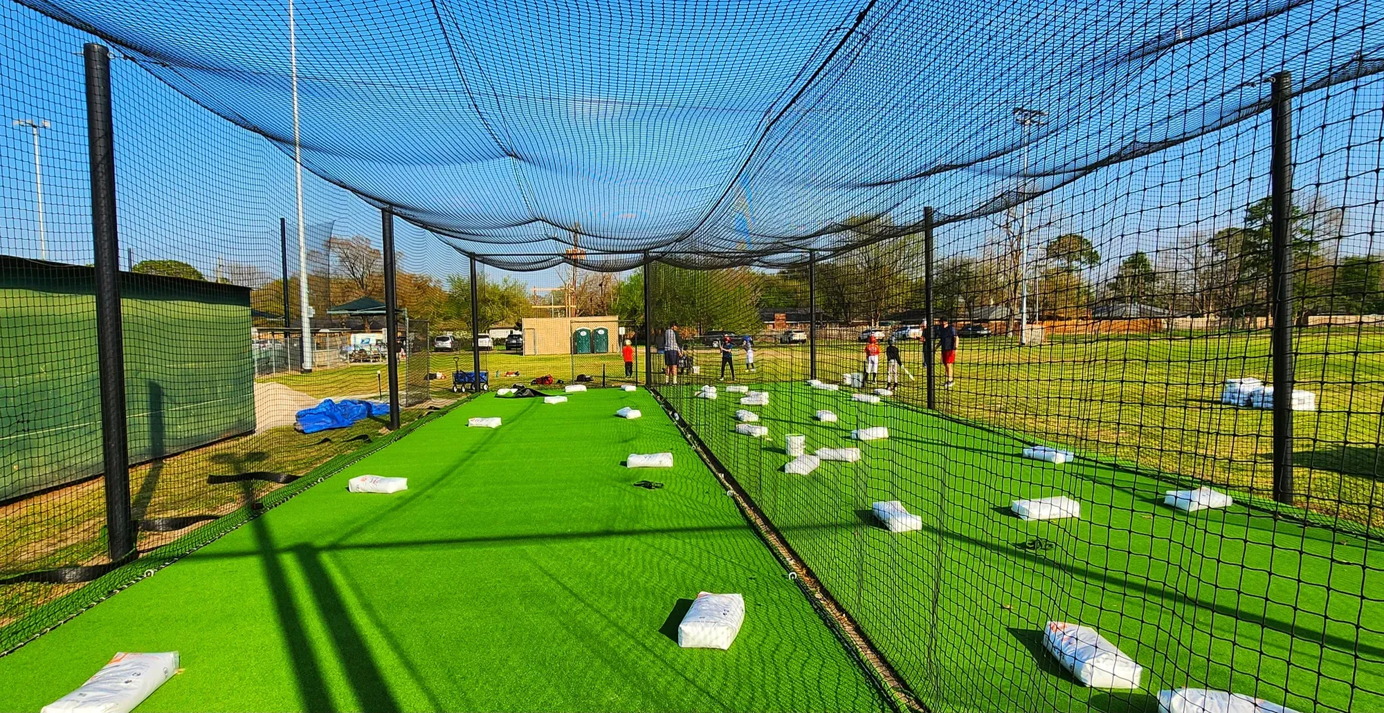Artificial turf floor inside a netted outdoor batting cage tunnel, the netting sloping overhead