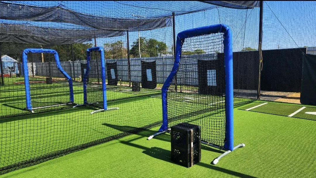 Outdoor netted batting cages with pitching machines, floored throughout in artificial turf