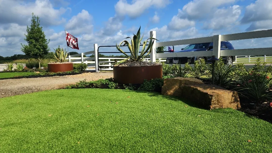 An artificial lawn running to a white ranch fence, with planted containers along its edge