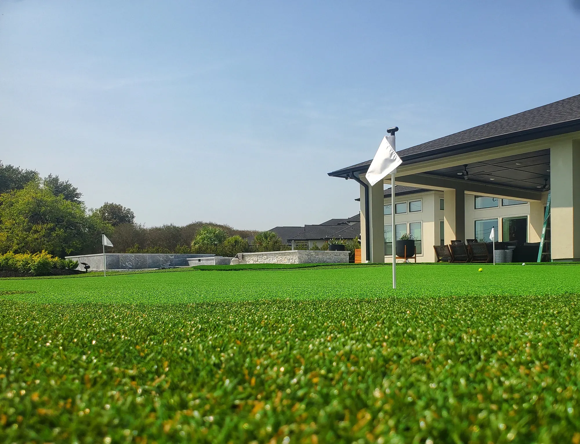 A wide practice green with a flagstick, house and covered patio beyond