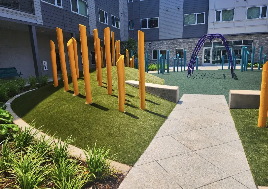 A playground courtyard with yellow posts and play arches on artificial turf beside a curved walk