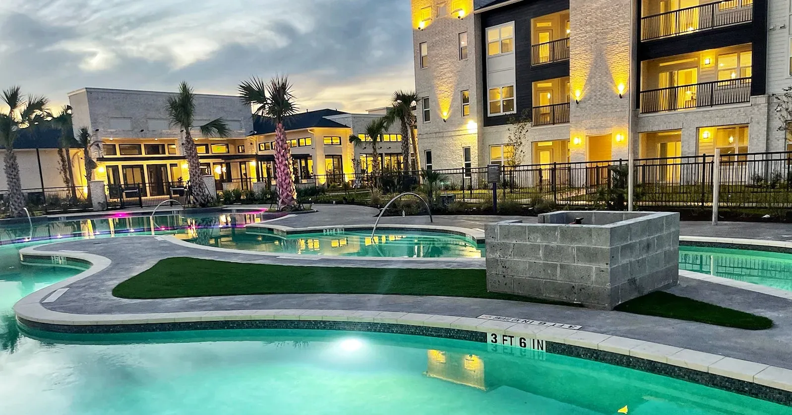 A lazy river pool lit at dusk, with an artificial turf island at its centre