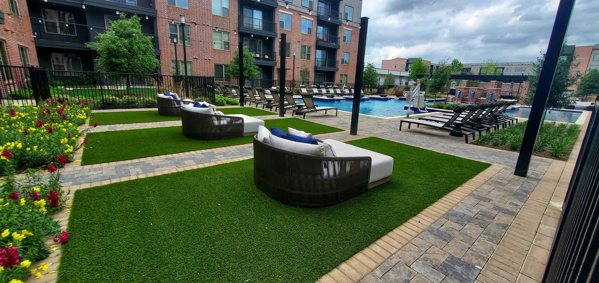 Apartment pool courtyard with artificial turf panels set between paver bands, curved daybeds on the turf and loungers along the pool