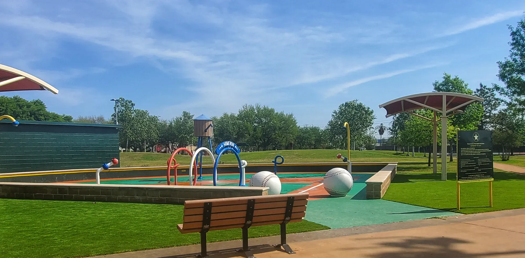 A municipal splash pad with colourful play features, surrounded by artificial turf and shaded seating