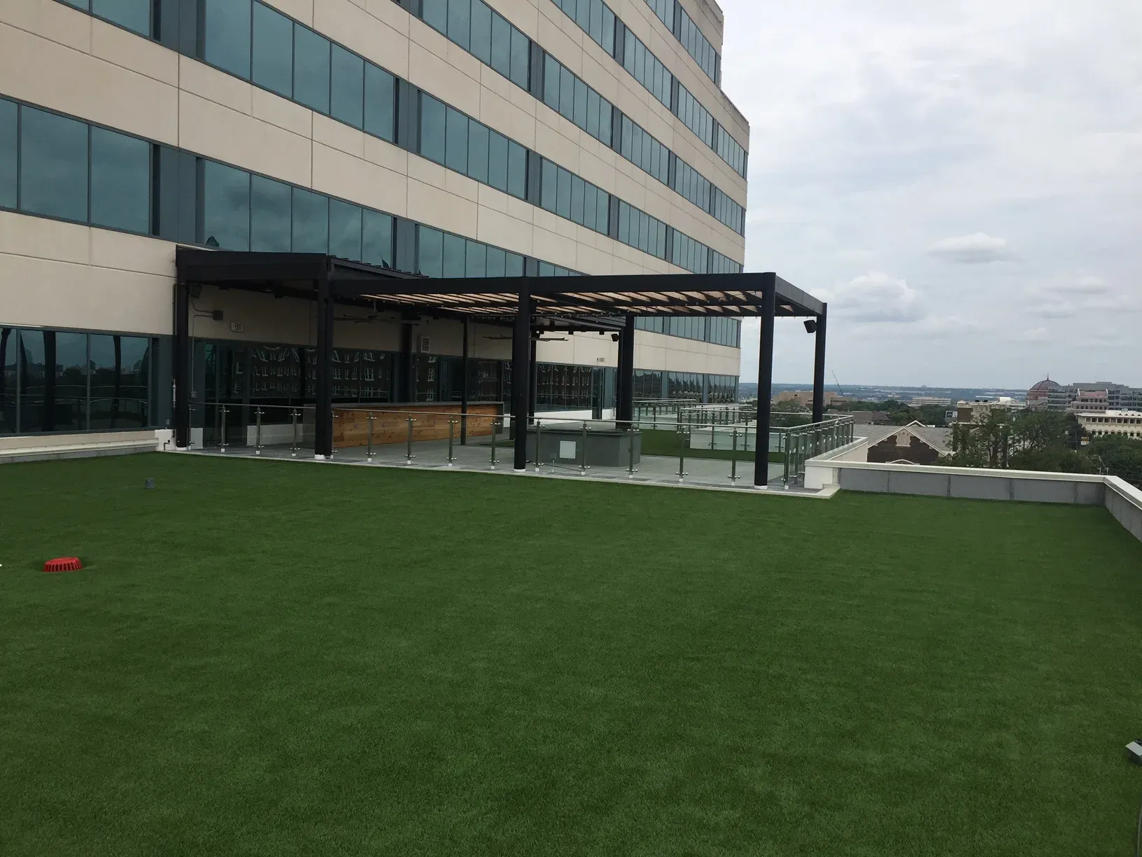 Large artificial turf lawn on an office tower roof terrace, with a pergola bar along one edge