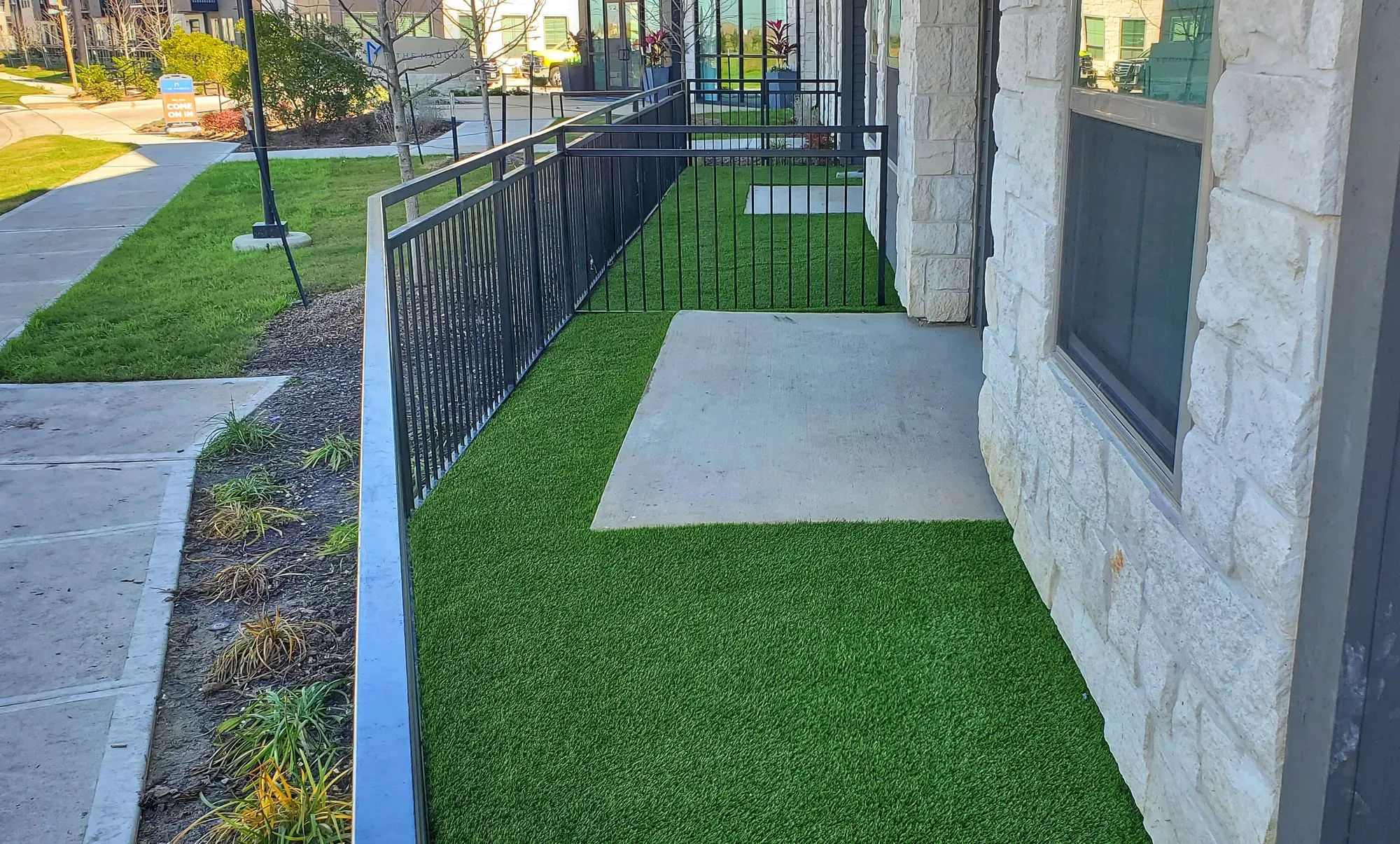 Artificial turf pedestrian run set with concrete pads, held between a building elevation and a metal rail