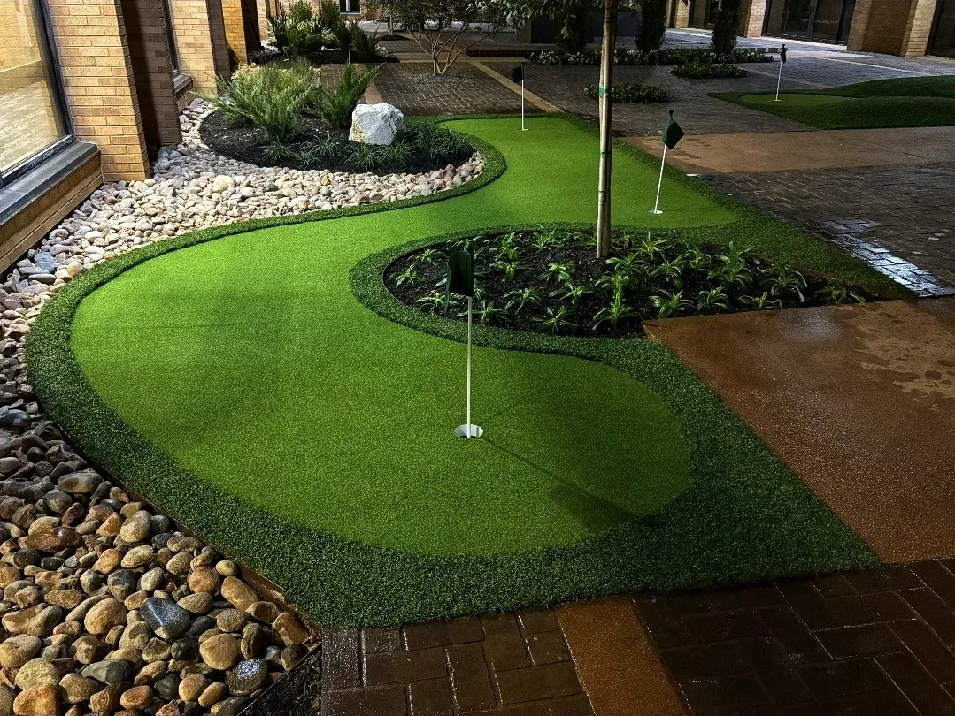 A curved courtyard putting green edged with river rock and a raised planter