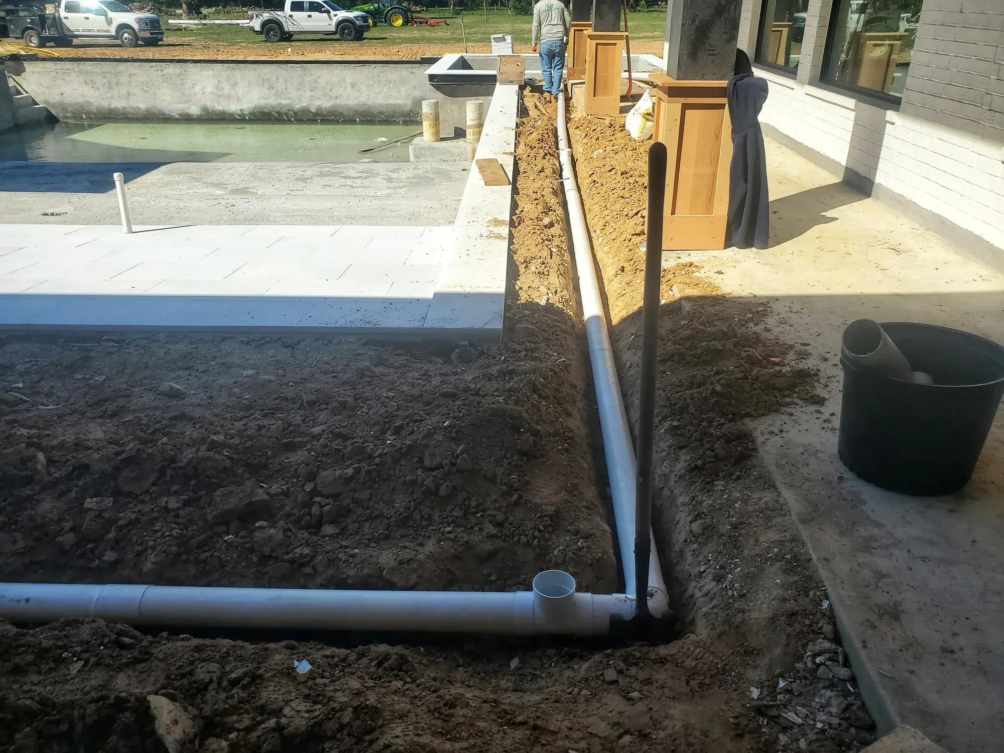 Open trench with white drain lines running the length of a pool deck on a job in progress