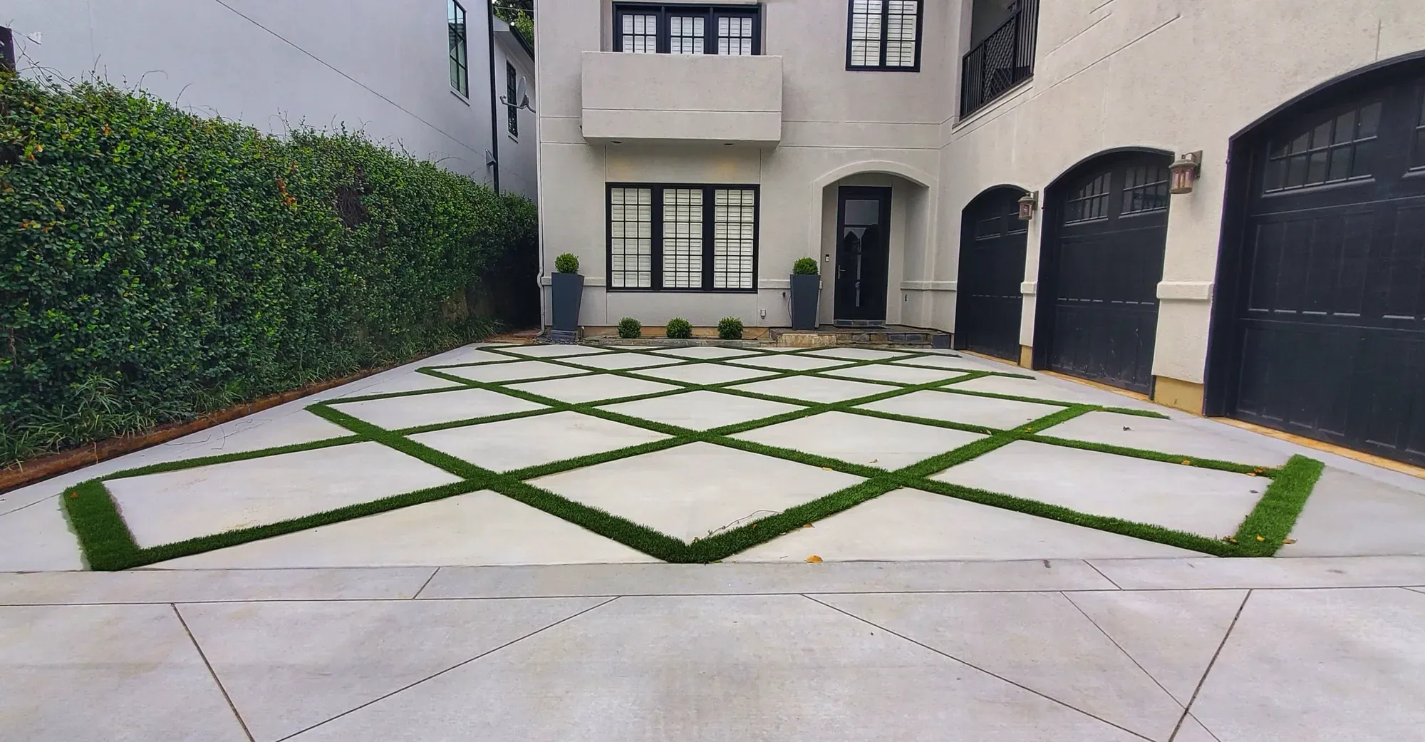 Front driveway laid as a diamond grid of concrete panels with artificial turf strips between them, in front of a house with three garage doors