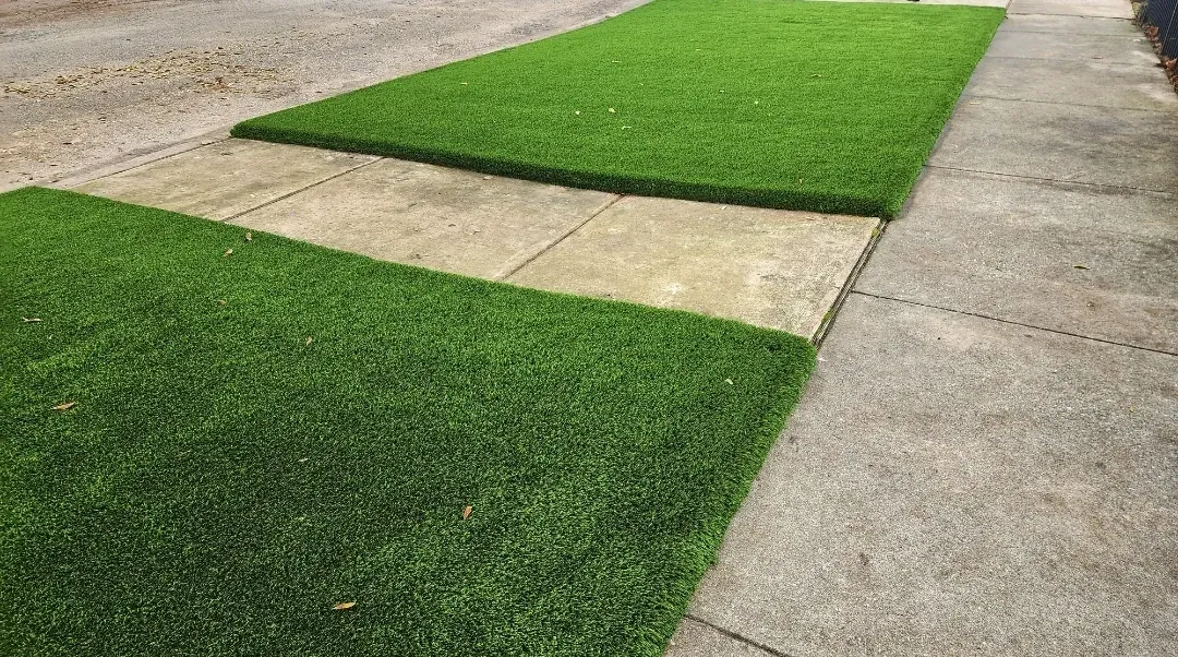 Two shades of artificial grass meeting either side of a concrete sidewalk