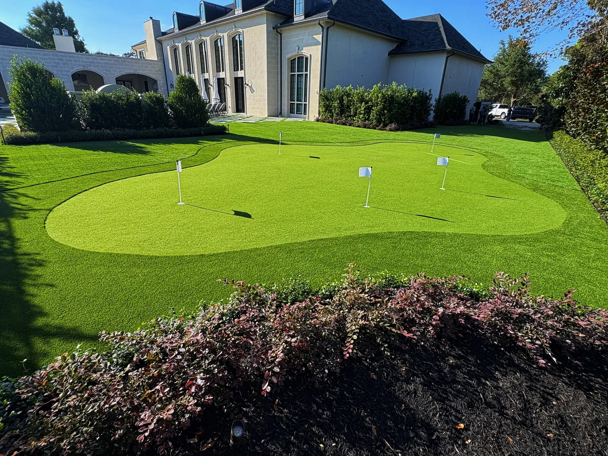 Five-flag artificial putting green with a curved fringe collar in front of a large house