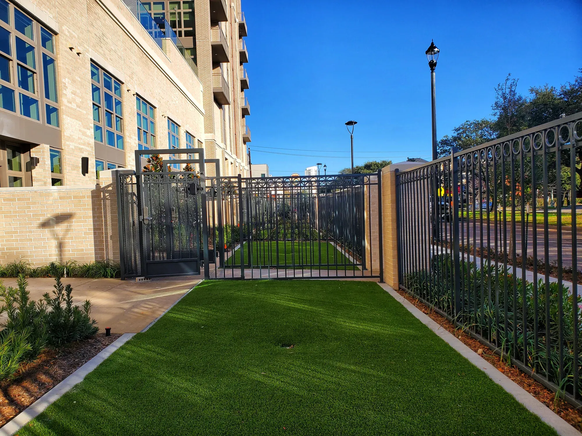 A gated front courtyard laid in artificial turf, seen through iron railings towards the street