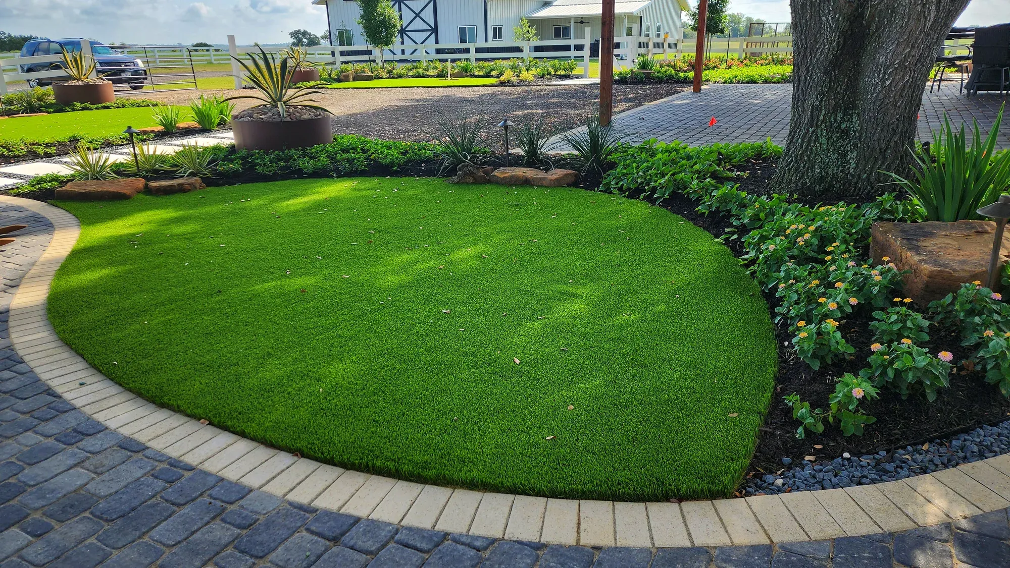 An artificial turf front lawn edged against a paver driveway and planting beds