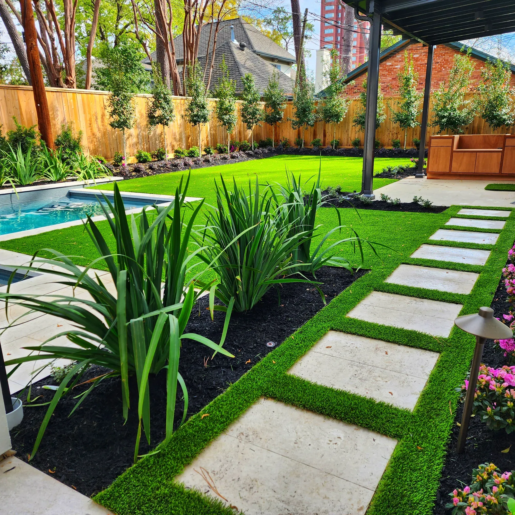 Square stepping stones set into turf strips through a planted garden beside a pool