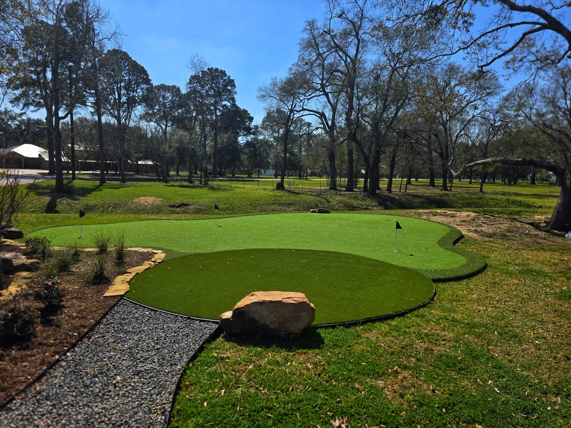 A large free-form practice green set into a lawn under mature trees