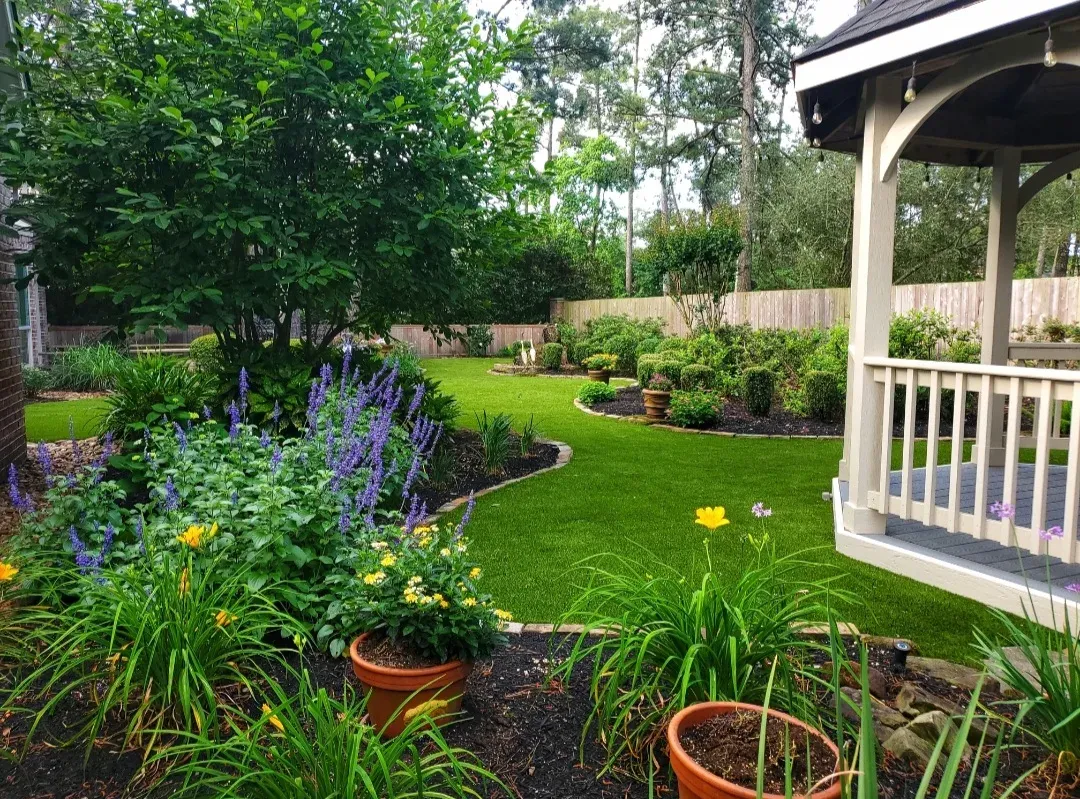A curving artificial lawn between deep flowering borders, with a white gazebo