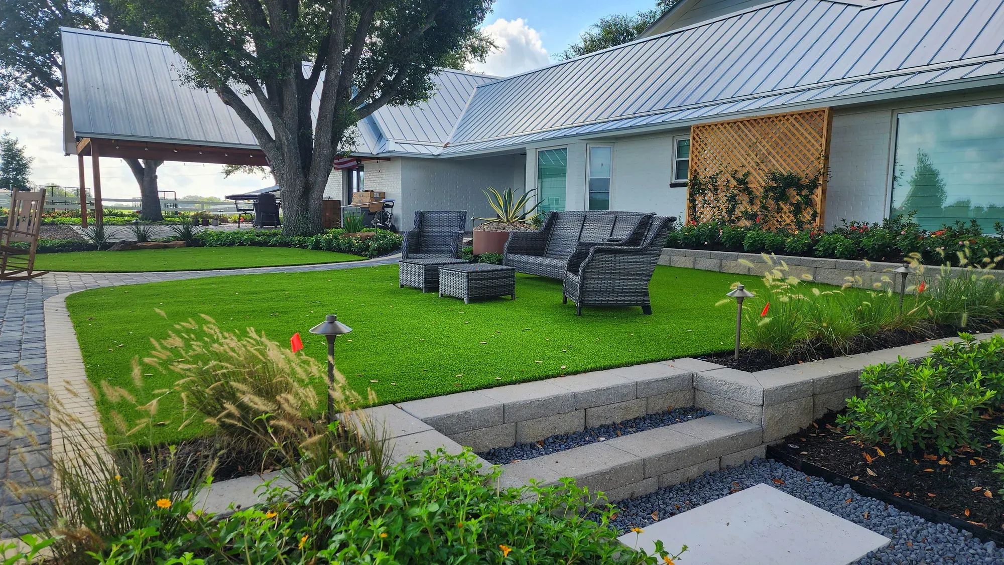 Wicker patio seating set on a manicured artificial lawn beside planting beds