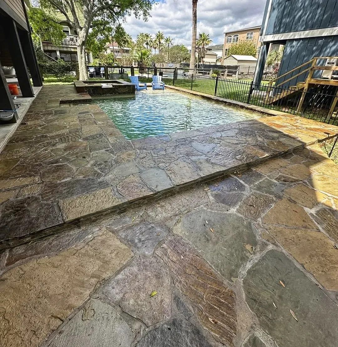 An irregular flagstone pool deck with artificial turf worked into the joints, beside a waterside pool