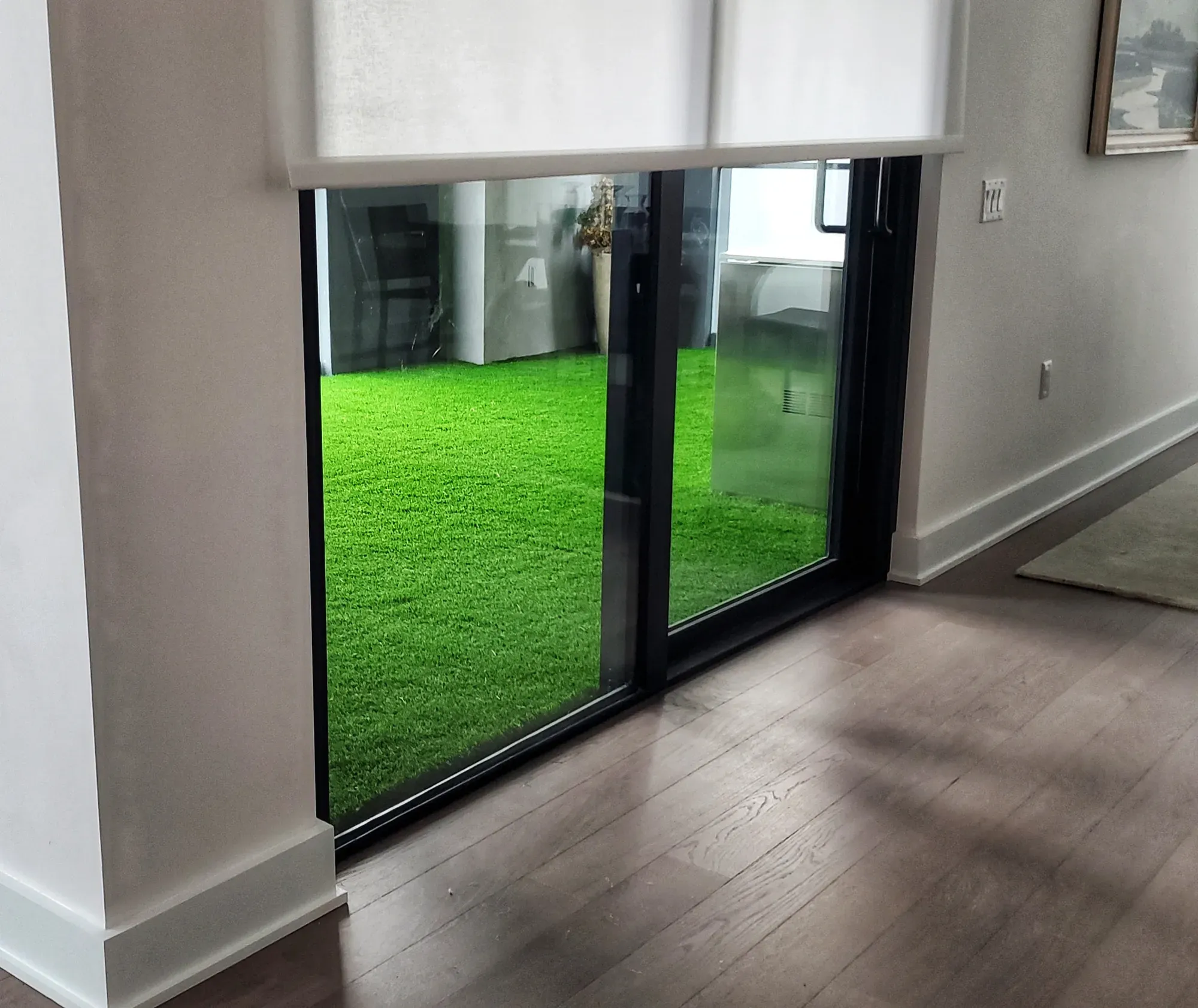 Artificial turf on a balcony, seen through a sliding glass door from inside