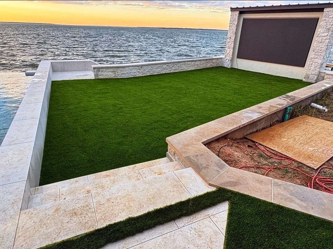 A stone-edged artificial turf terrace on the lake shore beside a covered seating area