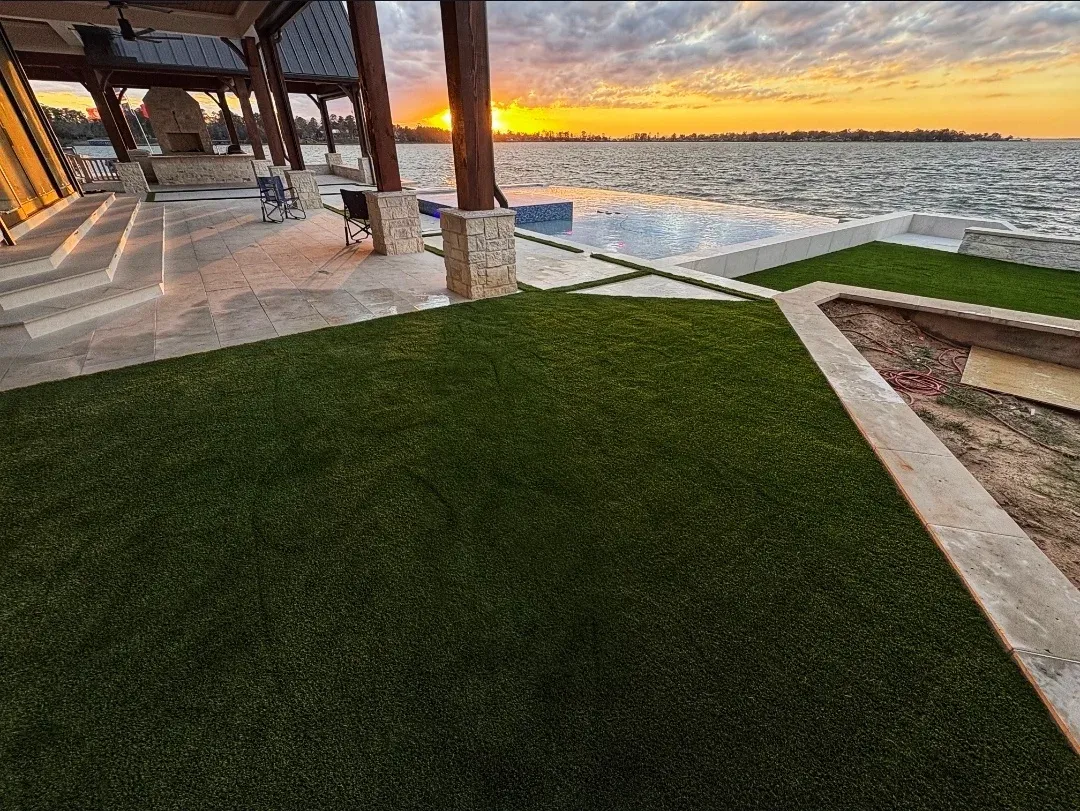A level artificial turf terrace under a covered patio, looking out over the lake at sunset