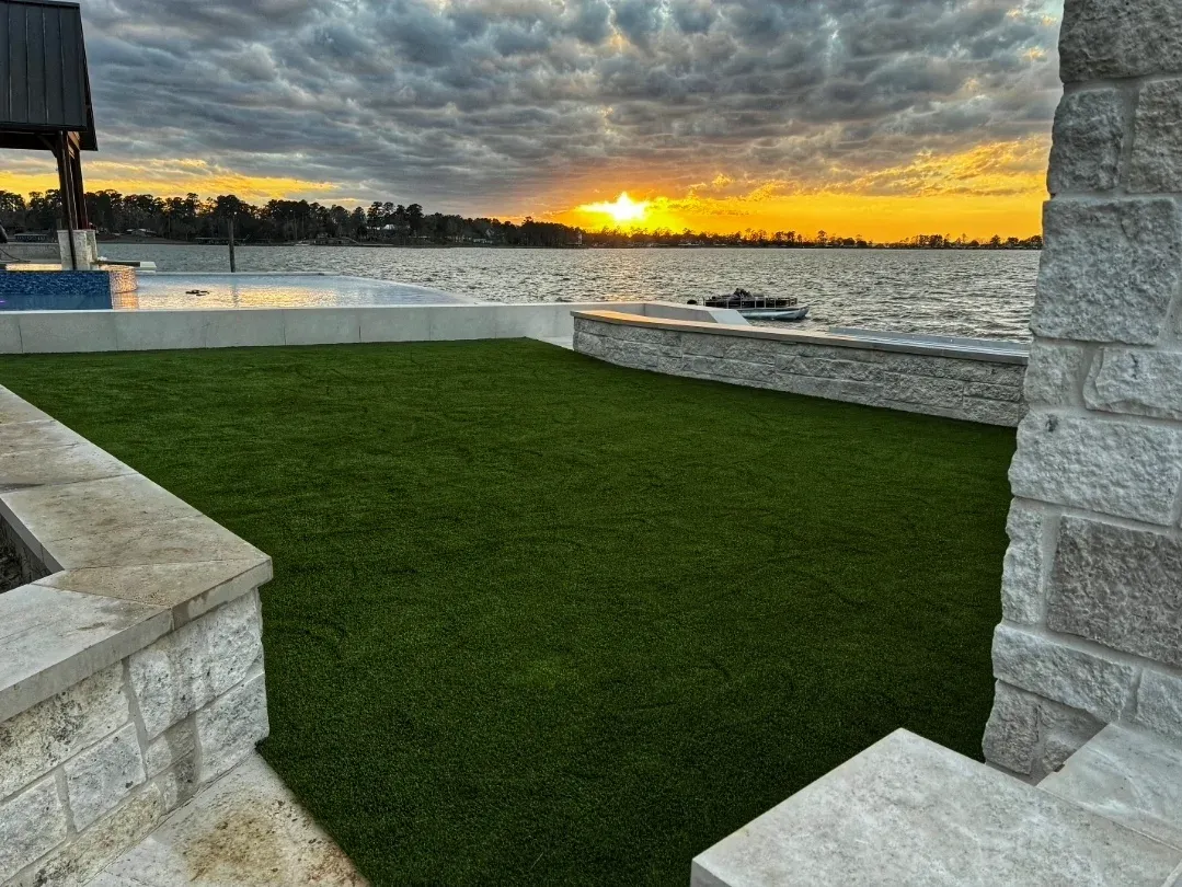 A lakeside turf terrace with a stone border, sun setting over the water