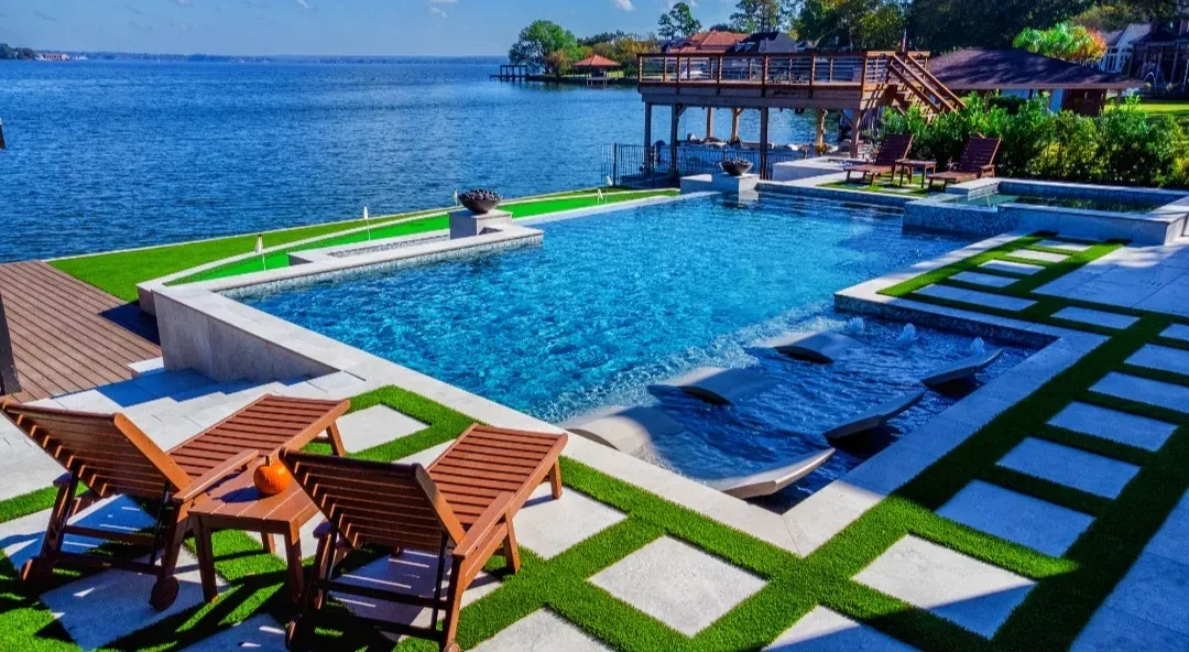 An infinity-edge pool overlooking the lake, with paver-and-turf strips across the deck
