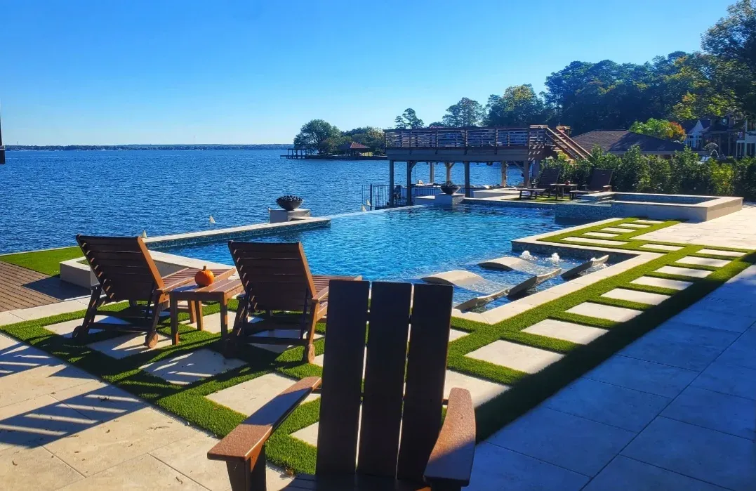 The infinity-edge pool from the deck, timber chairs on paver-and-turf strips