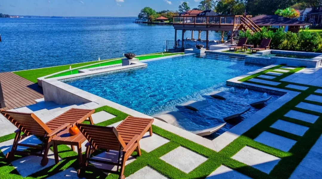 The infinity-edge pool looking out over the lake, paver-and-turf strips across the deck
