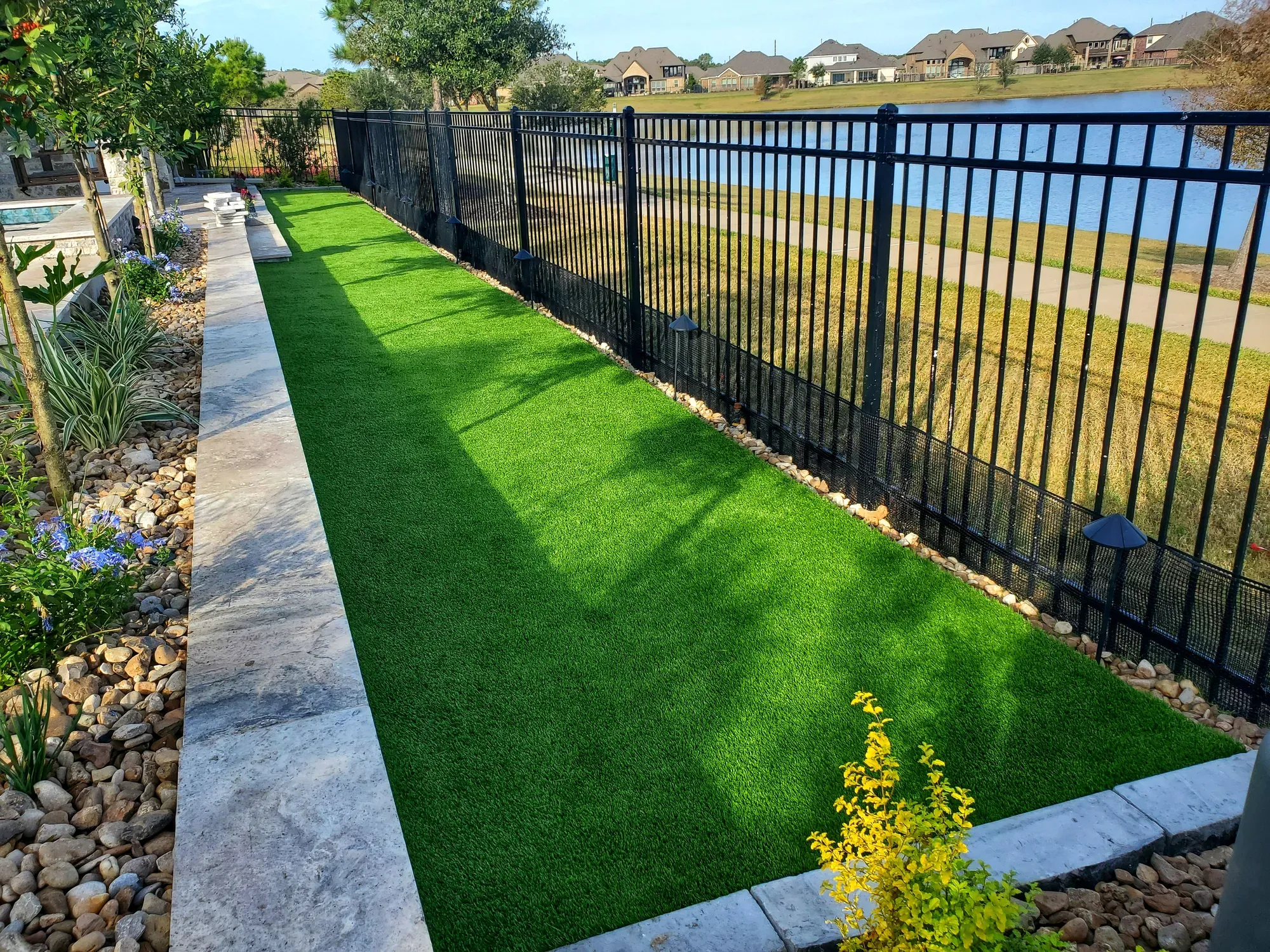 A narrow strip of artificial turf running along a black fence beside a lake