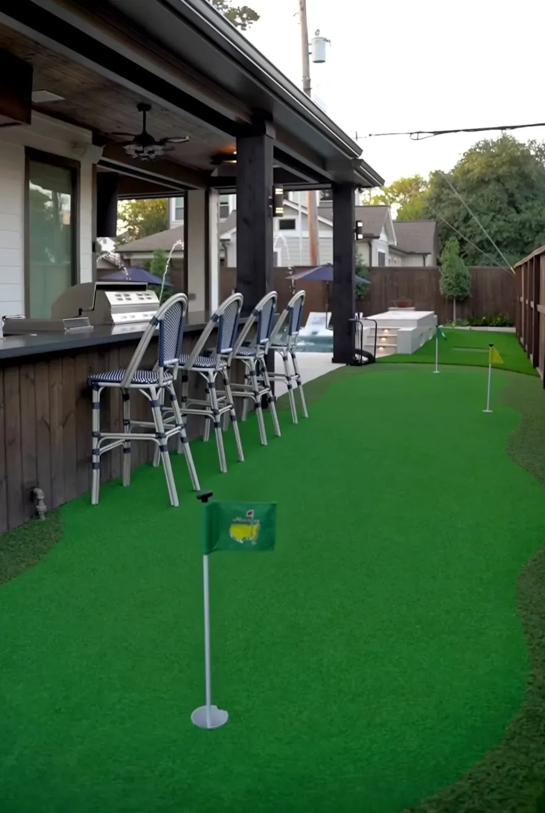 A practice green running under a covered patio and bar seating